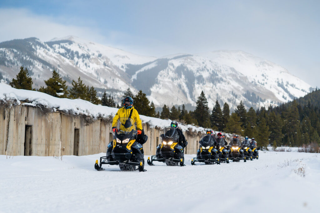 Snowmobile tour group with riders in line with alpine terrain in background