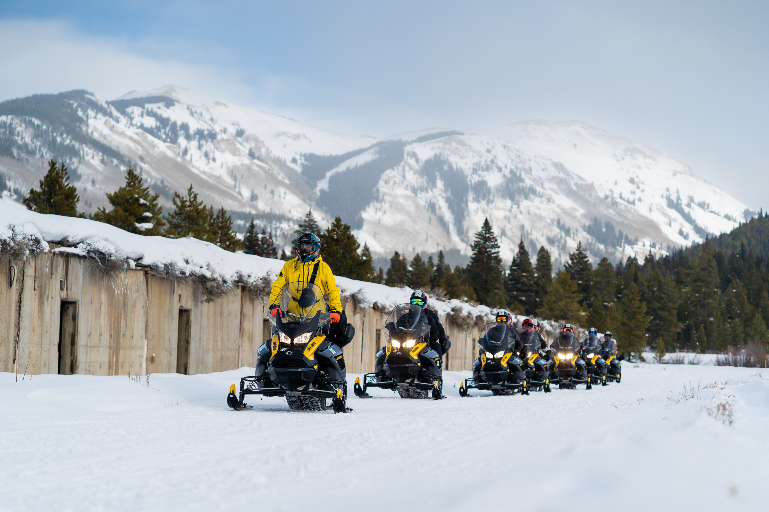 Snowmobile tour group with riders in line with alpine terrain in background